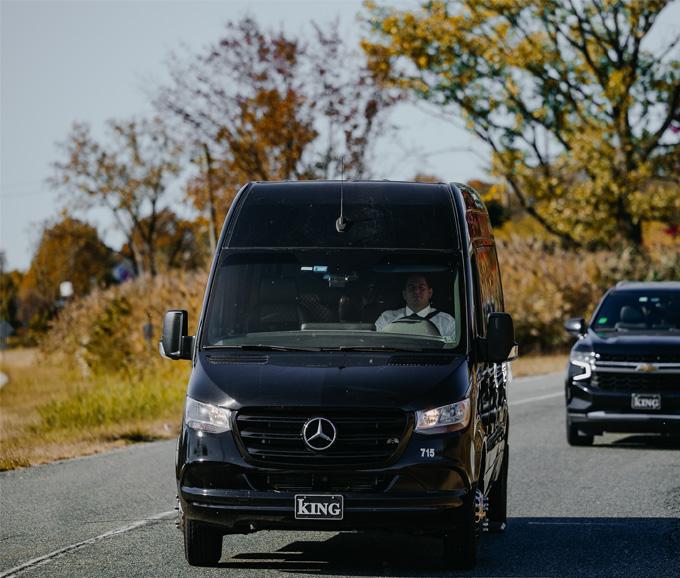Black van traveling down a road with a pickup truck following it
